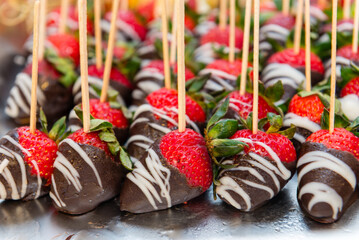 A tray of chocolate covered strawberries with wooden skewers