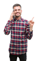 Canvas Print - Young hipster adult man talking on the phone very happy pointing with hand and finger to the side