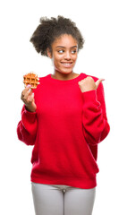 Wall Mural - Young beautiful afro american woman eating waffle over isolated background pointing and showing with thumb up to the side with happy face smiling