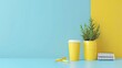 © lililia - A yellow coffee cup sits on a light blue surface next to a yellow planter with a leafy plant. A spiral notebook and two yellow pens are also on the surface