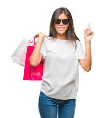 Sticker - Young asian woman holding shopping bags on sales over isolated background surprised with an idea or question pointing finger with happy face, number one