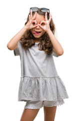 Canvas Print - Brunette hispanic girl wearing sunglasses doing ok gesture like binoculars sticking tongue out, eyes looking through fingers. Crazy expression.