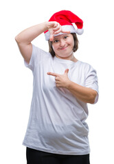 Canvas Print - Young adult woman with down syndrome wearing christmas hat over isolated background smiling making frame with hands and fingers with happy face. Creativity and photography concept.