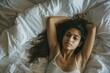 © vefimov - A woman is laying on a bed with her arms crossed. She has long hair and a serious expression on her face