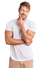 Wall Mural - Young caucasian man wearing casual white tshirt looking confident at the camera smiling with crossed arms and hand raised on chin. thinking positive.