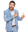 © Krakenimages.com - Young hispanic man wearing business jacket smiling and looking at the camera pointing with two hands and fingers to the side.