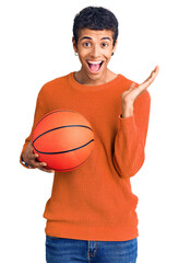 Wall Mural - Young african amercian man holding basketball ball celebrating victory with happy smile and winner expression with raised hands