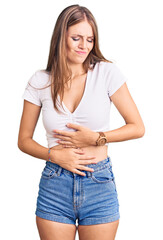 Wall Mural - Young beautiful blonde woman wearing casual white tshirt with hand on stomach because indigestion, painful illness feeling unwell. ache concept.