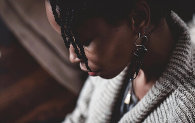 Wall Mural - A close-up portrait of an African American woman wearing braided hair and a grey knitted sweater, looking down and slightly to the left