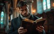 © imagineRbc - A church pastor sits inside a church, reading a leather-bound Bible. Warm lighting illuminates the scene, highlighting the worn pages of the book