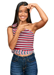 Wall Mural - Beautiful hispanic woman wearing casual clothes smiling making frame with hands and fingers with happy face. creativity and photography concept.