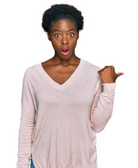 Wall Mural - Young african american girl wearing casual clothes surprised pointing with hand finger to the side, open mouth amazed expression.