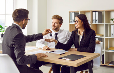 Professional man realtor giving house key to a woman client sitting in office. Young couple reaching agreement with a real estate agent, signed a contract enjoying real estate or car purchase.