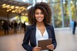 © JM Pixels - Happy professional using tablet near office building. Young African American business woman standing outside, holding digital device, looking at camera, smiling. Wi-Fi concept
