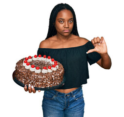 Poster - Young african american woman celebrating birthday holding big chocolate cake with angry face, negative sign showing dislike with thumbs down, rejection concept