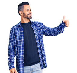 Canvas Print - Young hispanic man wearing casual clothes looking proud, smiling doing thumbs up gesture to the side