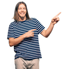 Sticker - Handsome caucasian man with long hair wearing casual striped t-shirt smiling and looking at the camera pointing with two hands and fingers to the side.