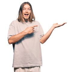 Sticker - Handsome caucasian man with long hair wearing casual clothes amazed and smiling to the camera while presenting with hand and pointing with finger.