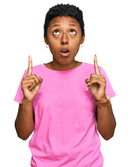 Wall Mural - Young african american woman wearing casual clothes amazed and surprised looking up and pointing with fingers and raised arms.