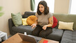 © Krakenimages.com - Hispanic woman working from home on laptop with a bottle of sanitizer on desk, expressing concern or problem-solving