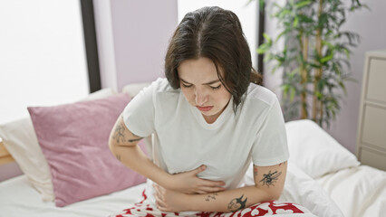 Canvas Print - A young caucasian woman experiencing stomach pain while sitting on a bed in a bedroom