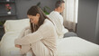 © Krakenimages.com - A woman and man sit apart on a bed in a bedroom, displaying tension or disagreement in their relationship.