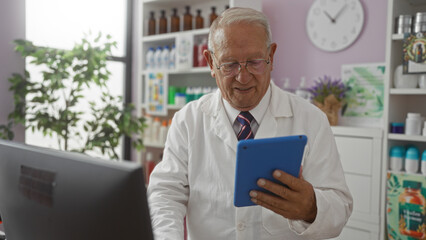 Wall Mural - A senior grey-haired caucasian man in a pharmacy wearing a white lab coat and glasses reading a tablet indoors.