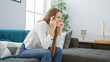 © Krakenimages.com - A cheerful young blonde woman sitting indoors on a sofa crossing her fingers in a home setting.