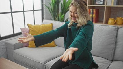 Wall Mural - Smiling young blonde woman stretching arms in a cozy living room setting, exuding casual elegance and comfort.