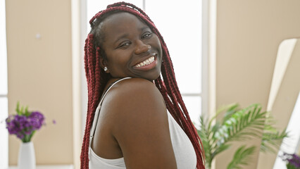 Poster - Smiling african american woman with braids in a relaxed indoor setting, exuding warmth and home comfort.