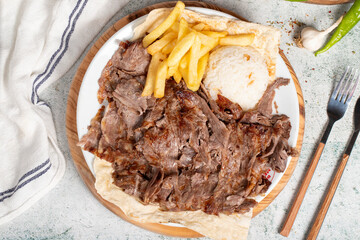 Meat doner with rice and French fries. Traditional Turkish cuisine taste. Meat doner kebab over rice cooked on a gray background. local name pilavustu et doner. Close up. Top view