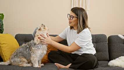 Canvas Print - Hispanic woman grooming adorable dog on a couch in a cozy living room setting.