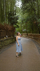 Poster - Beautiful hispanic woman with glasses, smiling confidently as she stands amongst kyoto's lush bamboo forest, looking around, full of joy and amazement.