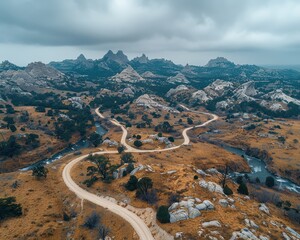 Wall Mural - Drone aerial view of winding road through rugged mountain landscape with dramatic clouds and rocky terrain on a cloudy day