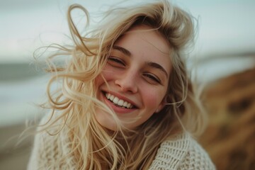 Poster - Radiant smile of a blonde woman as wind tousles her hair on a beach