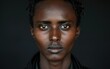 © imagineRbc - A close-up portrait of a young man with dark skin and braided hair, staring directly into the camera