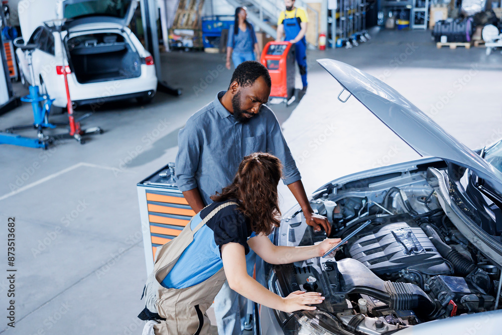 Skillful mechanic helping client with car checkup in auto repair shop ...