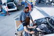 © DC Studio - Skillful mechanic helping client with car checkup in auto repair shop. Employee in garage facility looking over automobile parts with woman, mending her vehicle steering mechanism during inspection