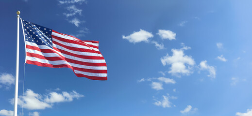 american flag on flag pole flying in the wind against blue sky with clouds