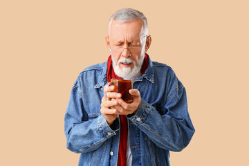 Wall Mural - Old man with sore throat holding cup of tea on beige background