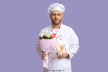 Canvas Print - Young male chef with flowers and gift box on lilac background. International Women's Day