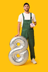 Canvas Print - Young male worker with balloon in shape of figure 8 and gift box on orange background. International Women's Day