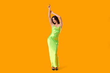 Wall Mural - Beautiful young woman in stylish green dress dancing on yellow background