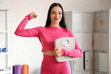 Sticker - Portrait of sporty young woman with scales showing muscles in gym