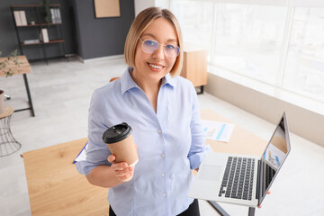 Wall Mural - Mature businesswoman with laptop and cup of coffee in modern office