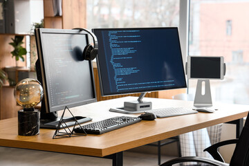 Wall Mural - computer monitors with programming code and headphones on desk in office