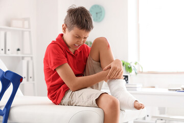 Wall Mural - Little boy with wounded knee sitting on couch in clinic