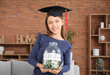 © Pixel-Shot - Teenage girl in mortar board holding jar with text COLLEGE at home. Tuition fees concept
