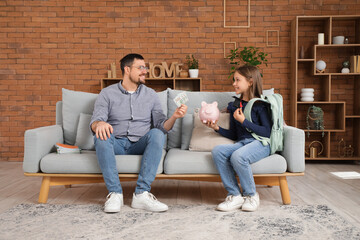 Poster - Father and his daughter holding piggy bank and money at home. Tuition fees concept