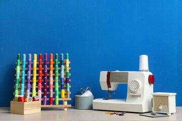 Sticker - Modern sewing machine with set of colorful threads and tailor's supplies on blue background